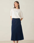 A woman modeling a white short-sleeve t-shirt and a dark navy blue denim midi skirt, paired with white sneakers, against a plain off-white studio background.